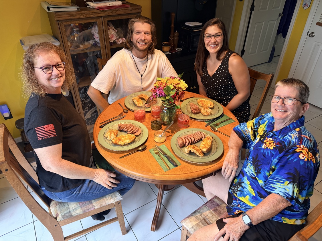 The group smiling around a table loaded with steak and chicken plates